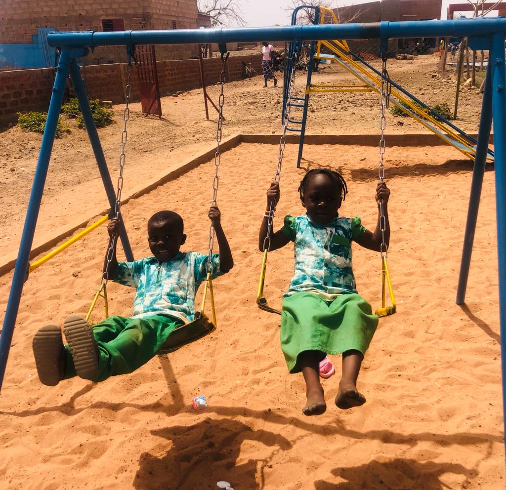 Zwei Kinder (ein Mädchen und ein Junge) aus dem Schulkomplex "Le Creuset d'Eveil" in Dédougou haben Spaß auf einer Schaukel.
